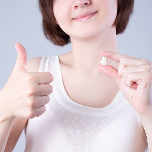 Nose-down view of woman holding extracted tooth giving thumbs up