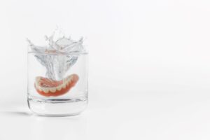 Set of dentures splashing into a glass of clear fluid with a white background