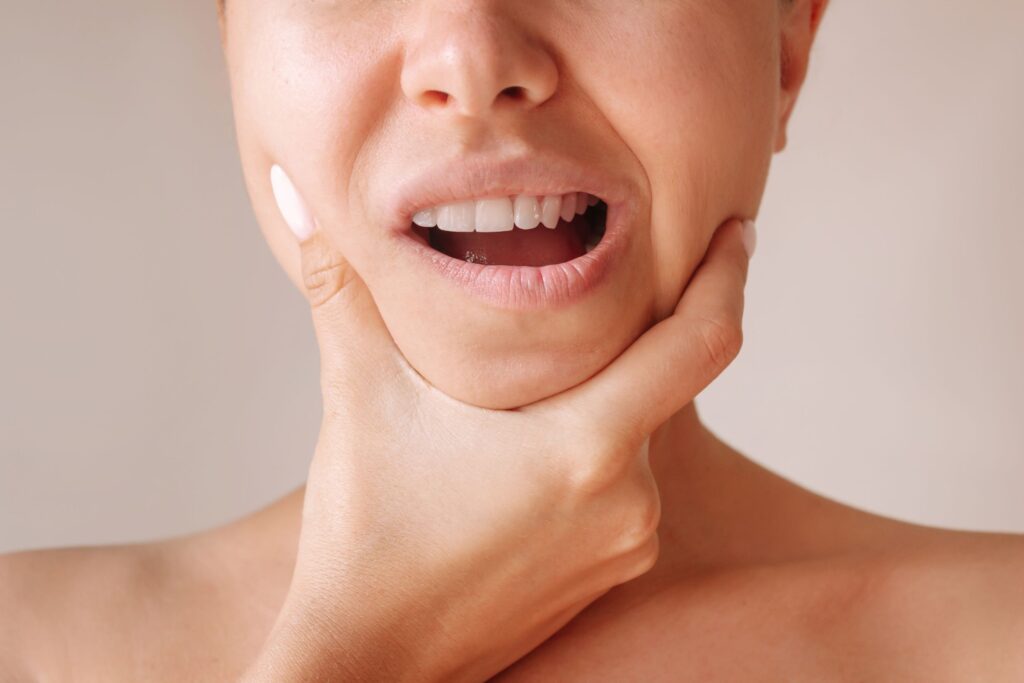 Nose down view of woman holding her sore jaw with thumb and pointer